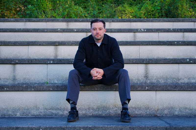 Theon Bower sitting on stone steps in Berlin, looking at the camera